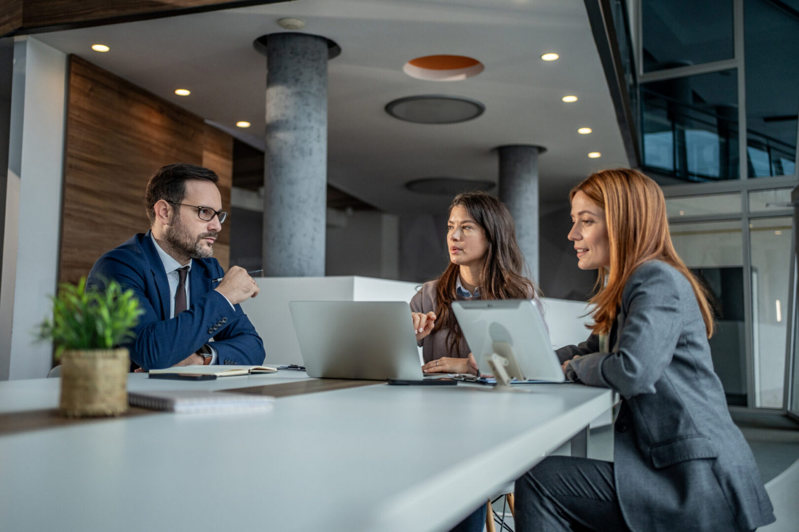 Three business people are discussing strategies and ideas while looking at laptops and a digital tablet, working together in a contemporary office setting