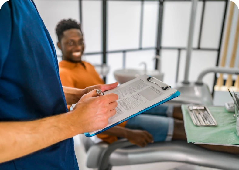 Dentist holding clipboard, patient in chair smiling.